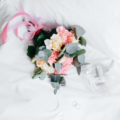 一束黄色和粉色的玫瑰和菊花放在白色纺织品上的范思哲喷雾瓶旁边